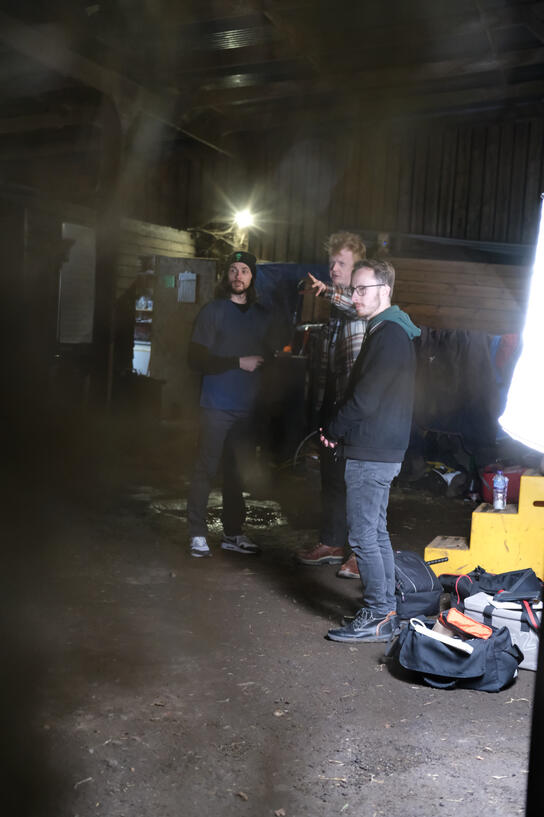 2 camera crew and one actor stand next to light on set